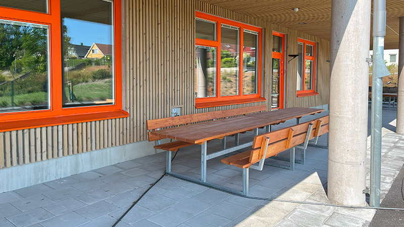 En sittgrup med bänkar och bord i trä utanför en byggnad.