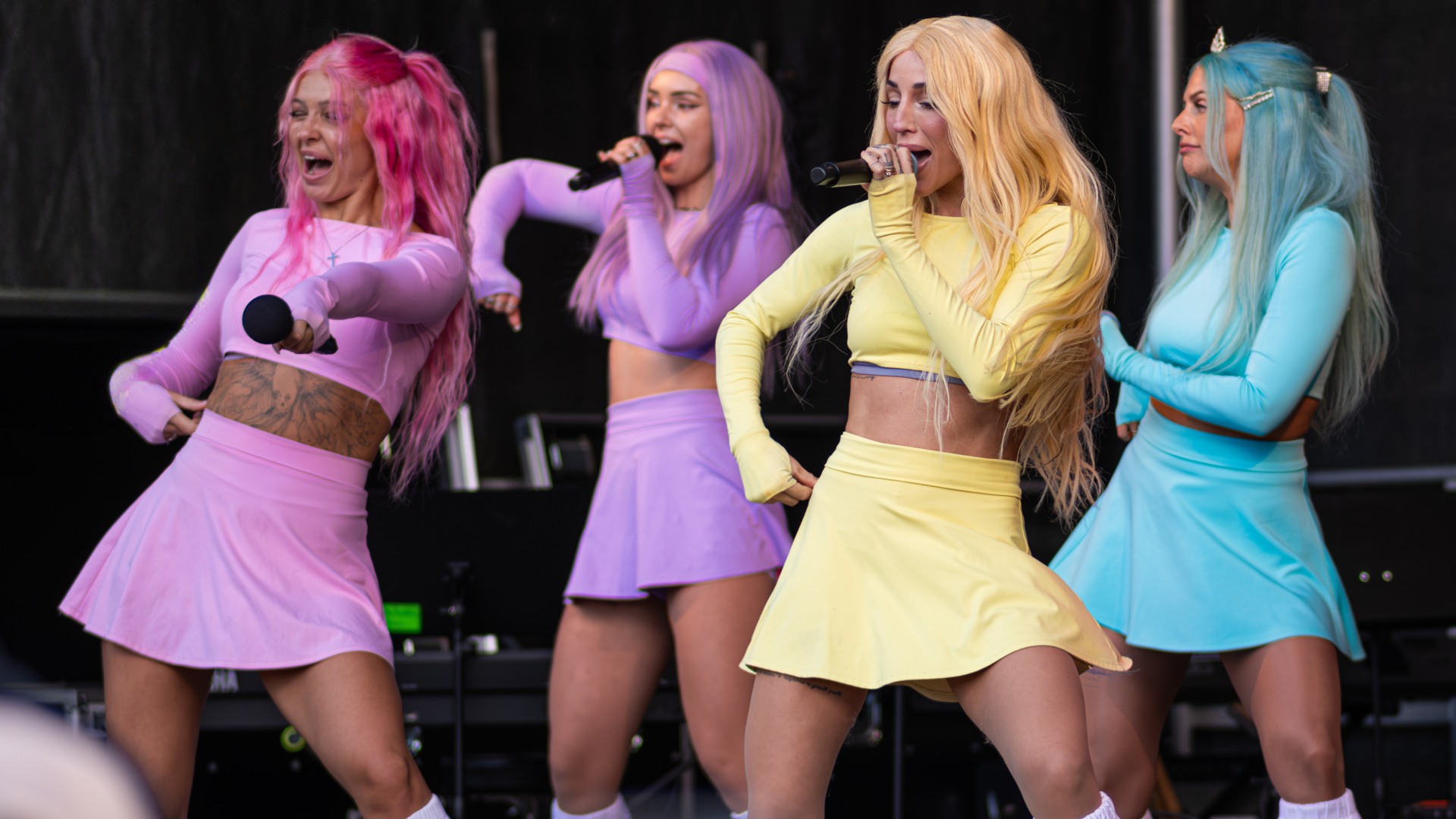 Fyra tjejer i pastelkläder uppträder på en scen.