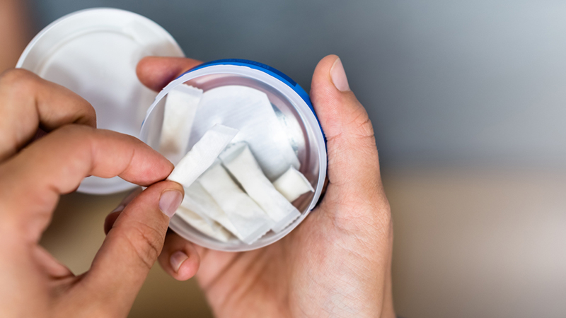 Händer som håller i en öppen dosa med vitt portionssnus.