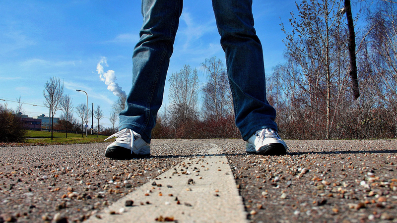 Jeansklädda ben med vita gympaskor står på en grusig gångbana