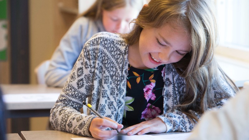 Ung flicka sitter vid skolbänk och skriver