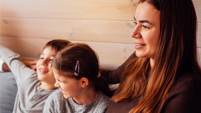 En kvinna med två barn sitter i soffa.