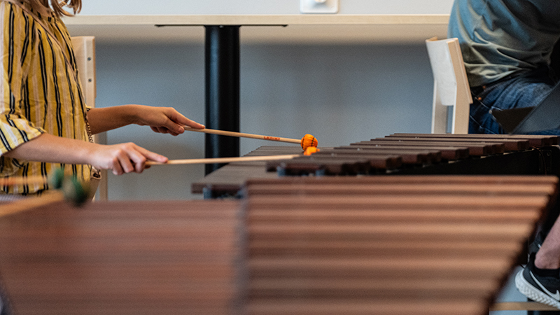 En person håller i något som liknar trumpinnar över ett klaviaturinstrument.