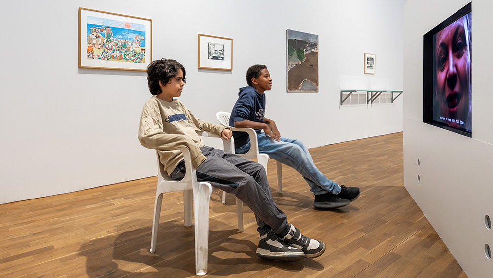 Två tonårskillar sitter och tittar på digital konst i en konsthall.