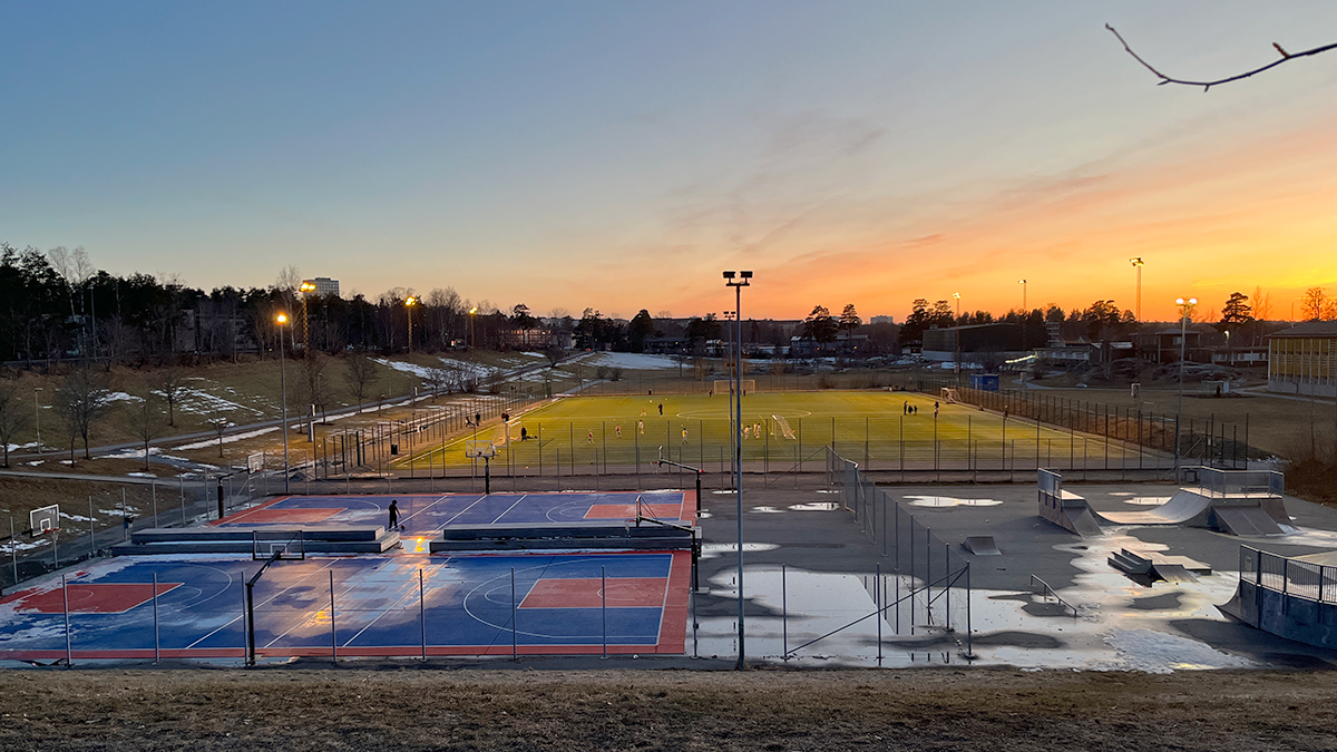 Vy över Vendelsömalmsgropens baskeplan, fotbollsplan och grönytor i solnedgång