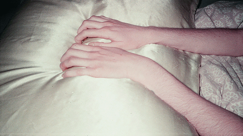 Två armar ligger på ett täcke, fotograferade i stillhet. Bilden ingår i konstutställningen "There was a wound; we dwelled".