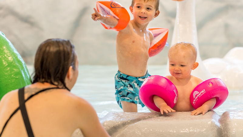 Två små barn leker i en pool med sin mamma